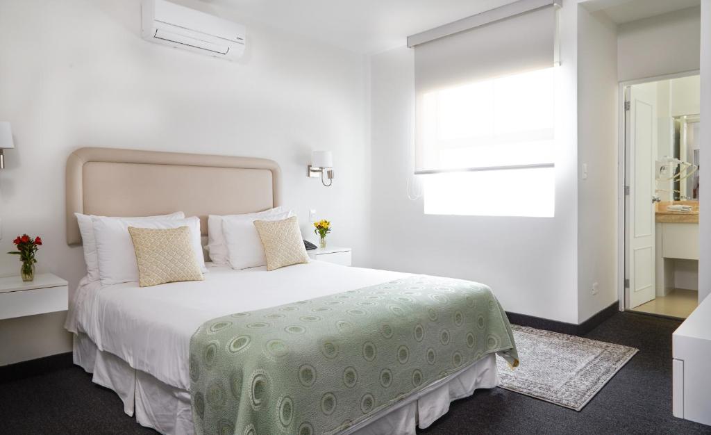 a white bedroom with a large bed with a green blanket at El Golf Hotel Boutique in Lima