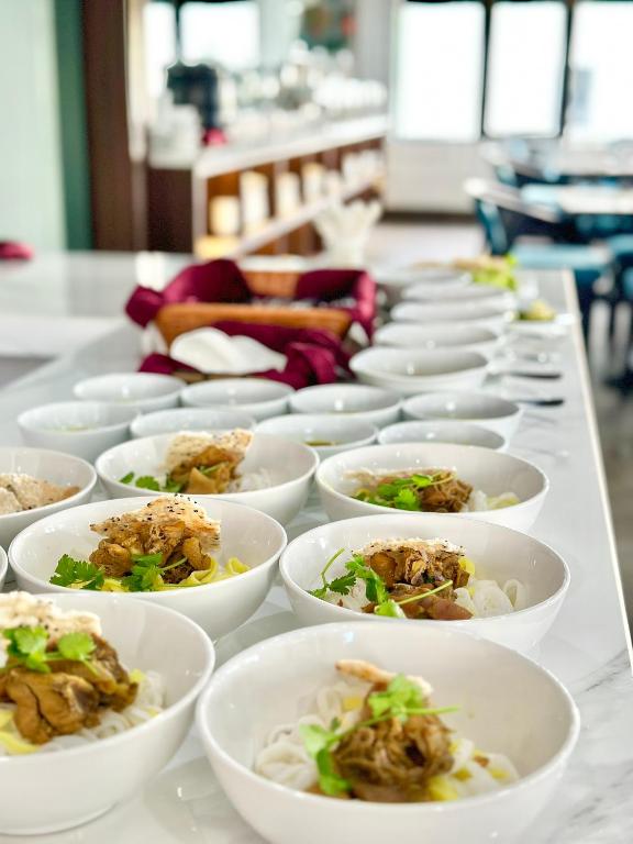 A long buffet table is lined with prepared noodle bowls.