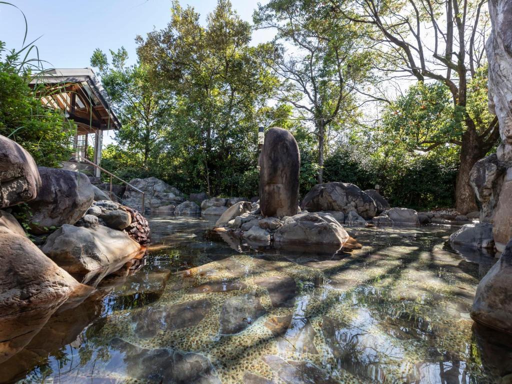 a pond in a garden with rocks and a statue at Tennenonsen Harunonoyu in Kochi