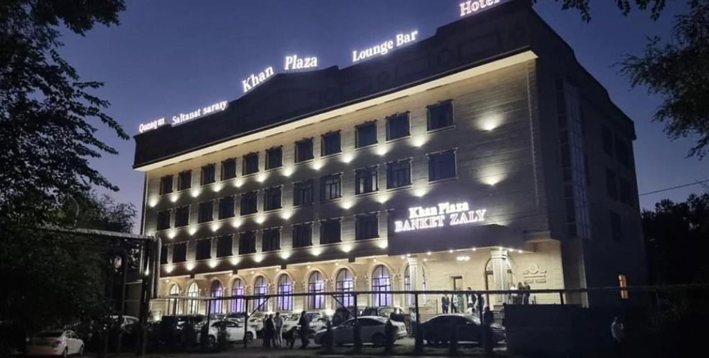 un edificio iluminado con coches estacionados frente a él en Khan Plaza en Almaty