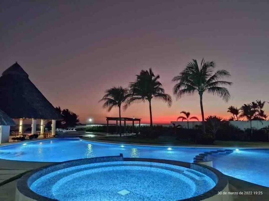 a resort pool with a sunset in the background at Hermoso Apartamento con club de playa in Acapulco