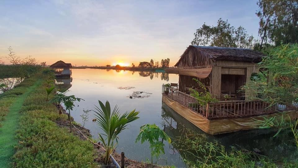 ein Haus auf einem Fluss mit Sonnenuntergang im Hintergrund in der Unterkunft Farmstay Ao Nhà 