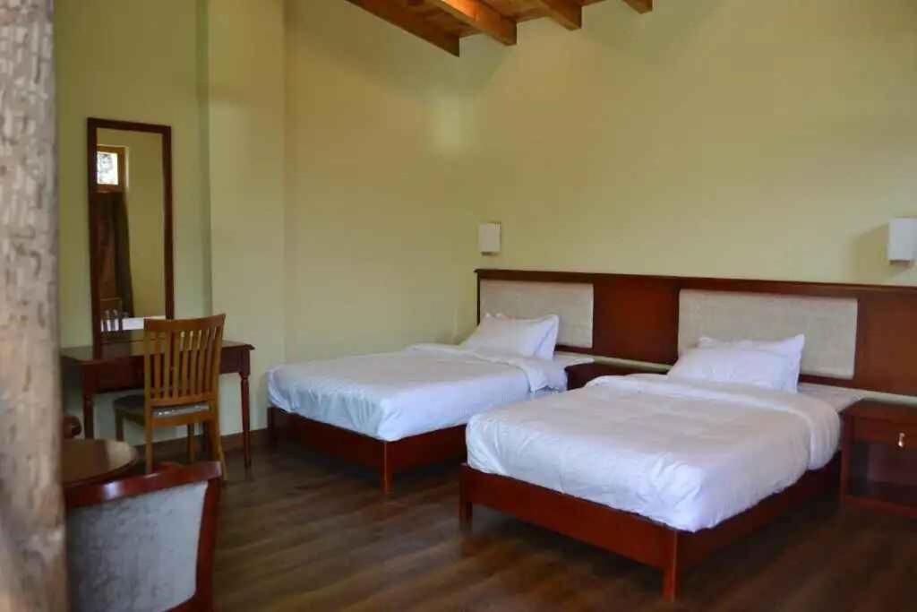 a bedroom with two beds and a table and a chair at Zhingkham Cottages in Thimphu