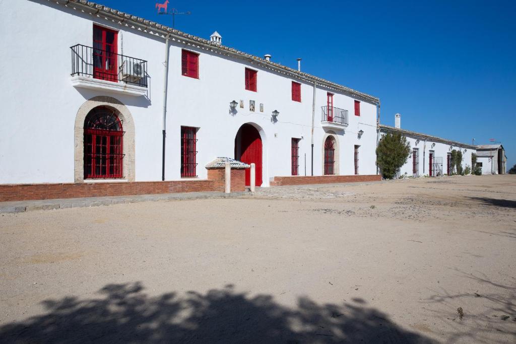a large white building with red doors and windows at CORTIJO RURAL LA MARISCALA in Jerez de la Frontera