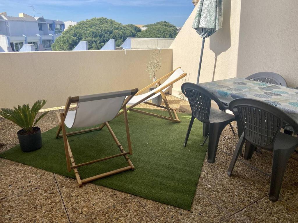 un patio avec une table et des chaises sur un tapis vert dans l'établissement SUPERBE STUDIO 4 PERSONNES - TERRASSE- PARKING- PISCINE, au Grau-du-Roi