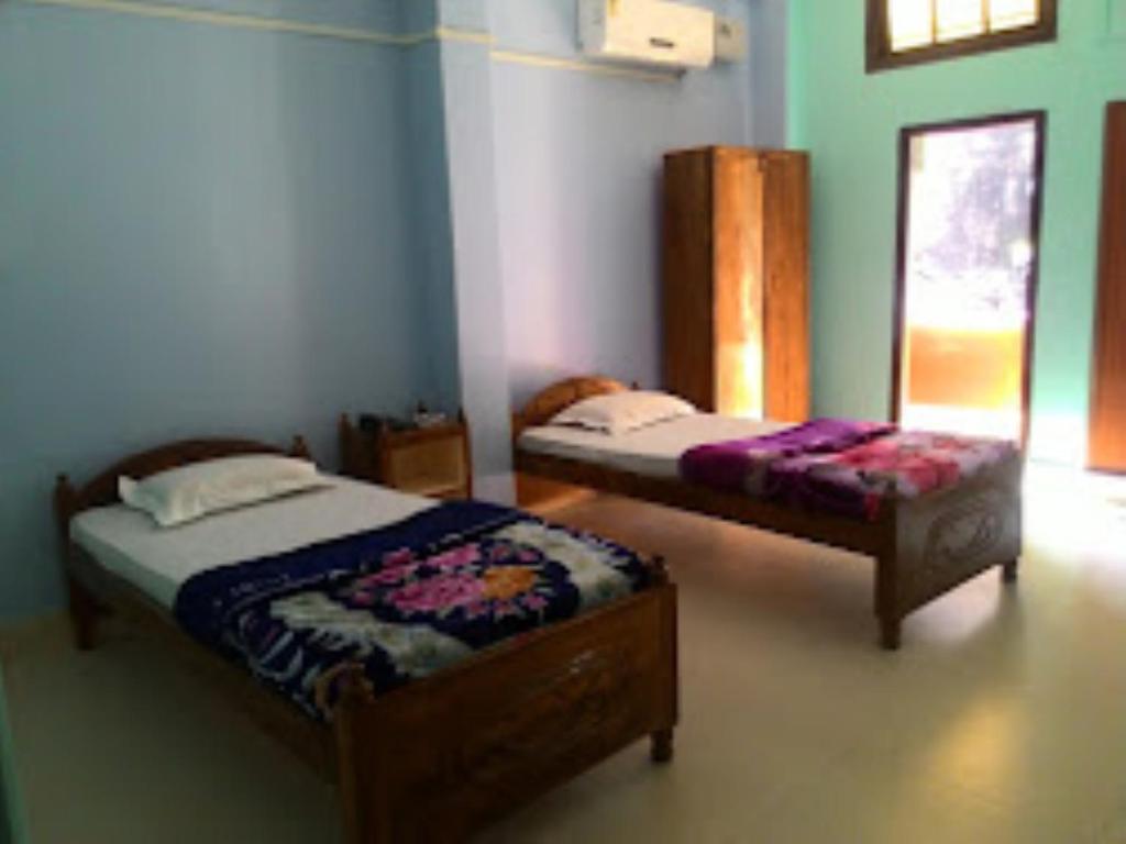 Sewak Lodge Silchar في سيلكار: غرفة نوم بسريرين ومقعد فيها