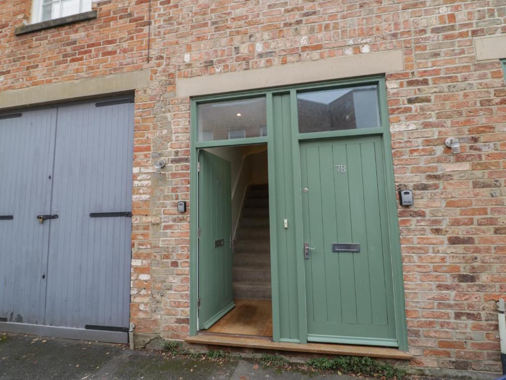 zielone drzwi w ceglanym budynku z dwoma drzwiami garażowymi w obiekcie 7A Lansdown Place Lane w mieście Cheltenham