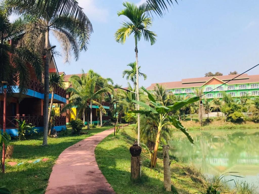 un chemin en face d'un complexe avec des palmiers dans l'établissement Saensukkho Green Hotel & Resort, à Chiang Rai