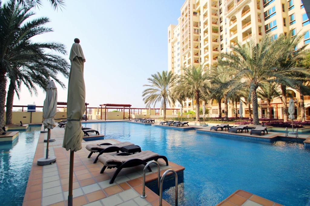 uma piscina com cadeiras e guarda-sóis e palmeiras em Sea and Atlantis View 3 BR Apartment Palm Jumeirah em Dubai