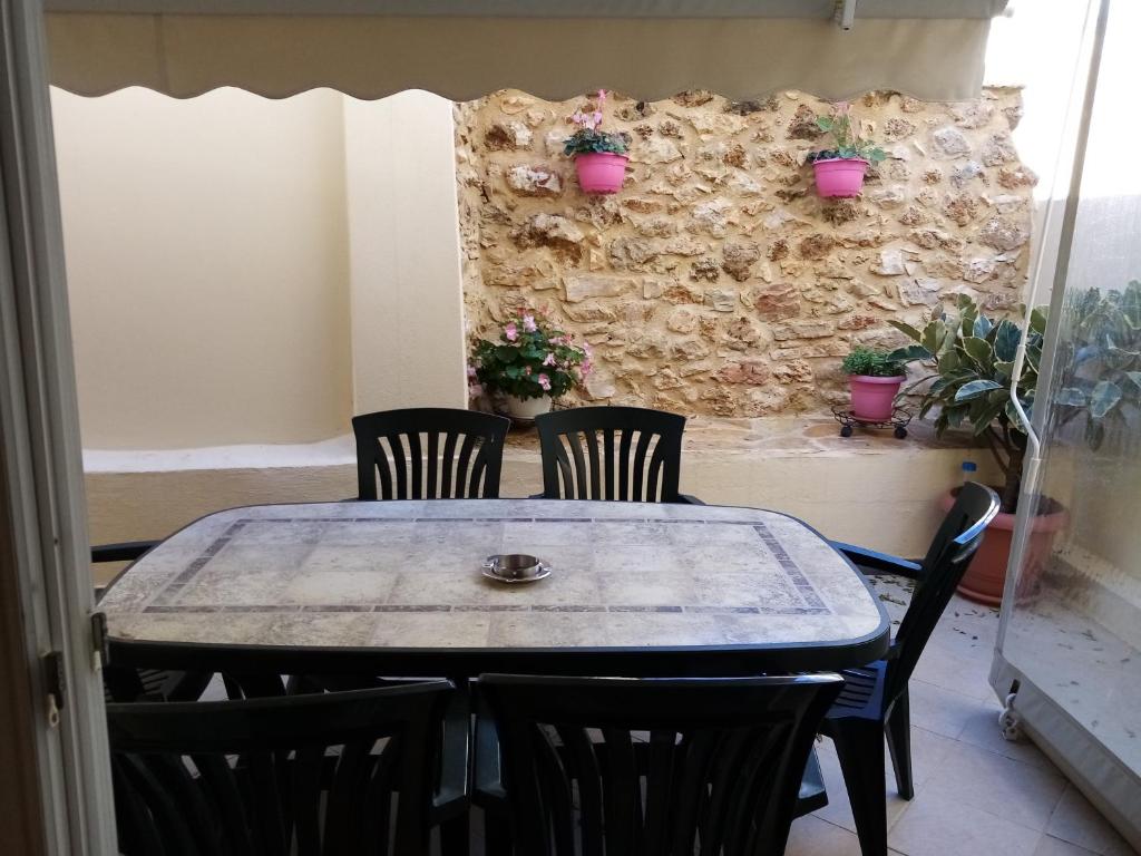 een tafel met stoelen en een stenen muur met potplanten bij Olga's House in Preveza
