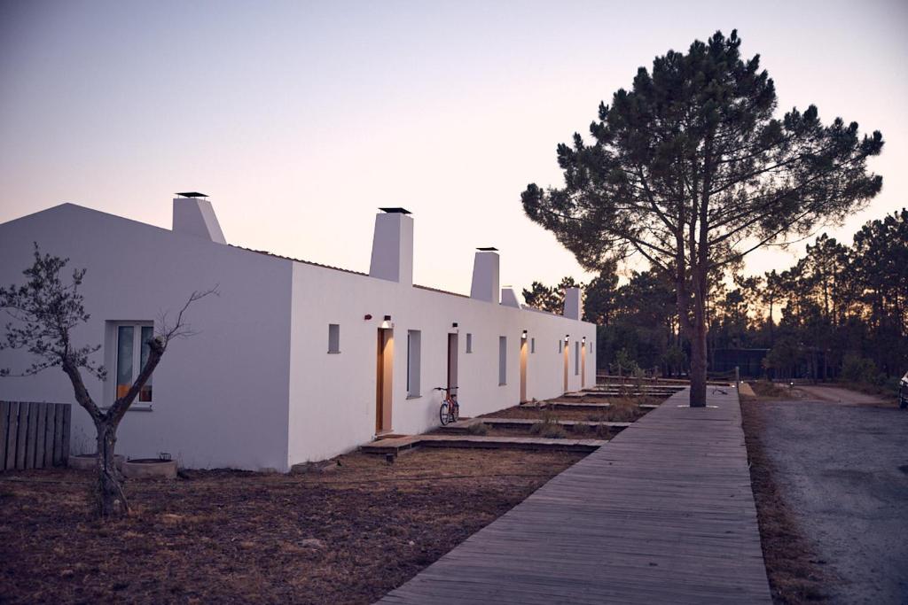 a white building with a wooden walkway in front of it at Craveiral Farmhouse by Belong Staying & Feeling in São Teotónio