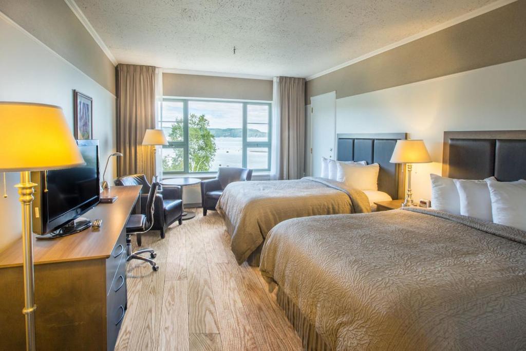 a hotel room with two beds and a desk with a television at Hôtel le Manoir Baie-Comeau in Baie-Comeau