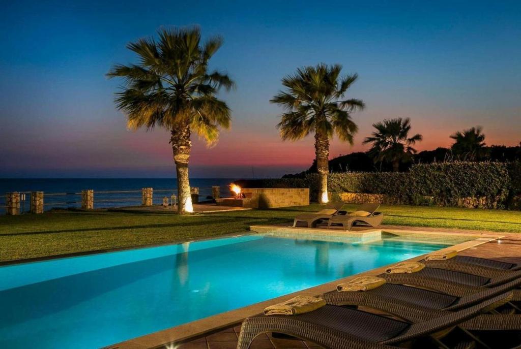 a swimming pool with chairs and palm trees at Astounding Seafront Kefalonia Villa - 3 Bedrooms - Villa Alegria - Private Pool and Amazing Sea Views - Minies in Kefallonia