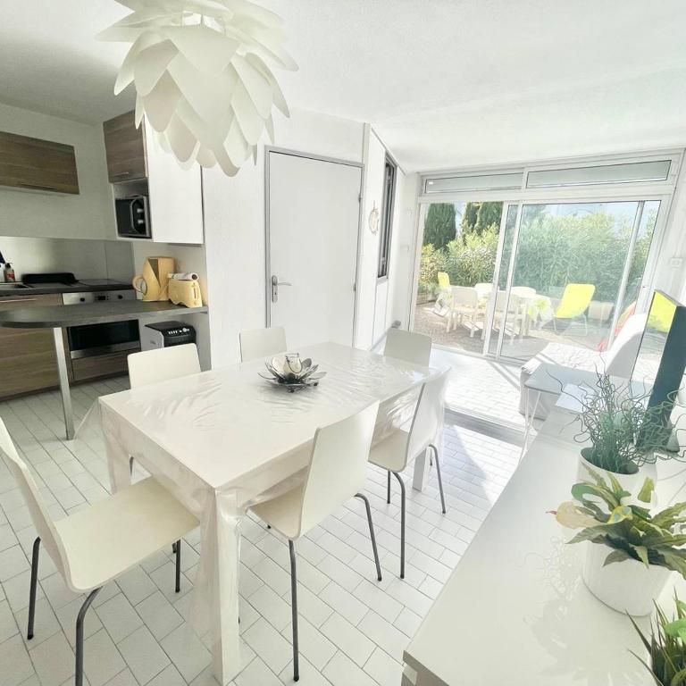une cuisine et une salle à manger avec une table et des chaises blanches dans l'établissement SECTEUR SEAQUARIUM - APPARTEMENT 6 PERS CLIMATISE RDC, 1 CHAMBRE - GRANDE TERRASSE, au Grau-du-Roi