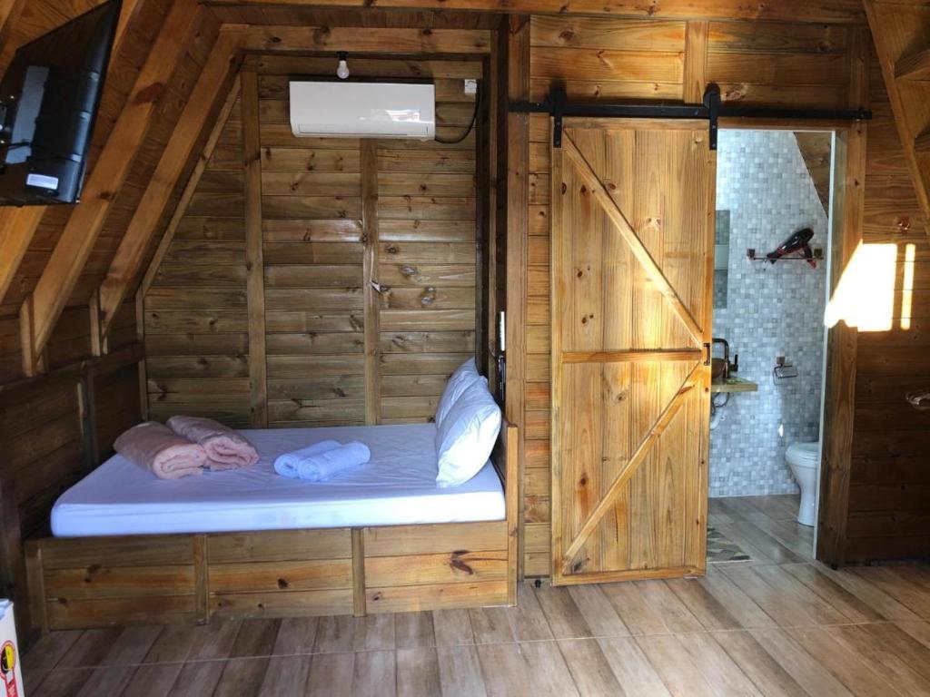 een klein bed in een houten kamer met een badkamer bij RECANTO VERDES VALES in Palhoça
