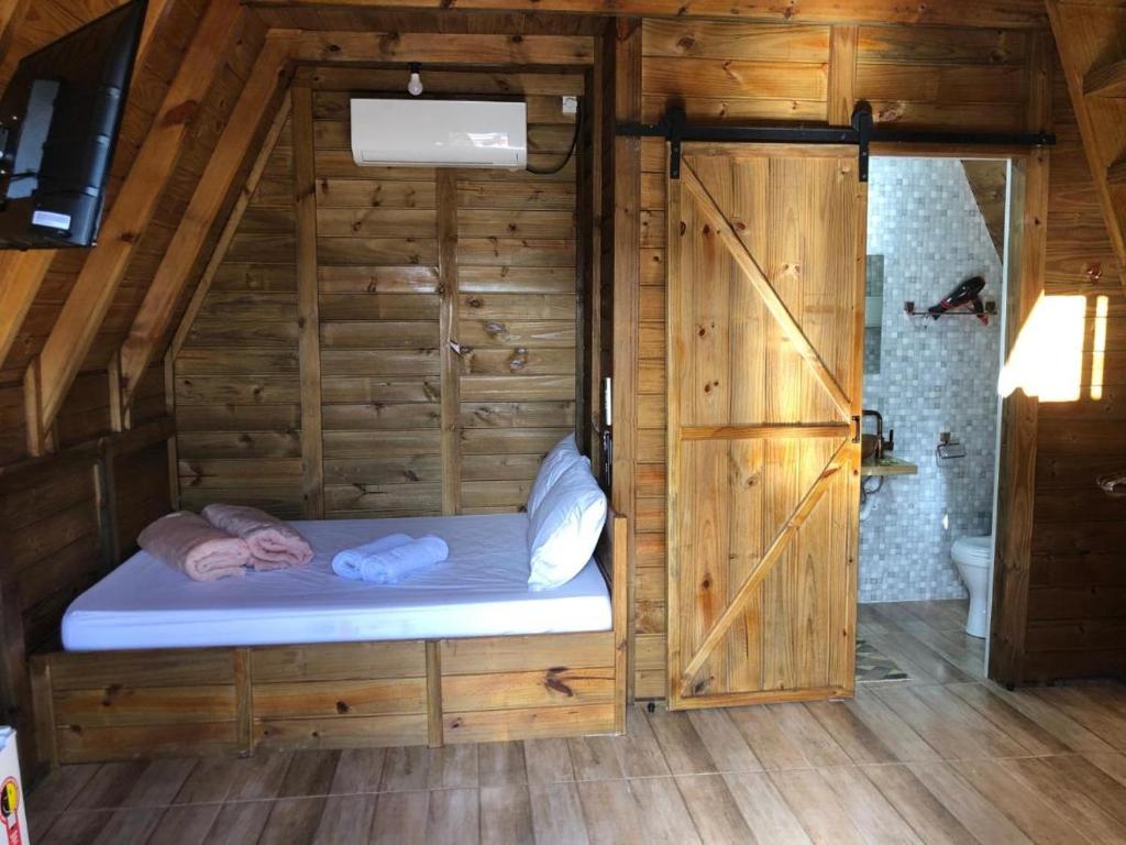 a small bed in a wooden room with a bathroom at RECANTO VERDES VALES in Palhoça