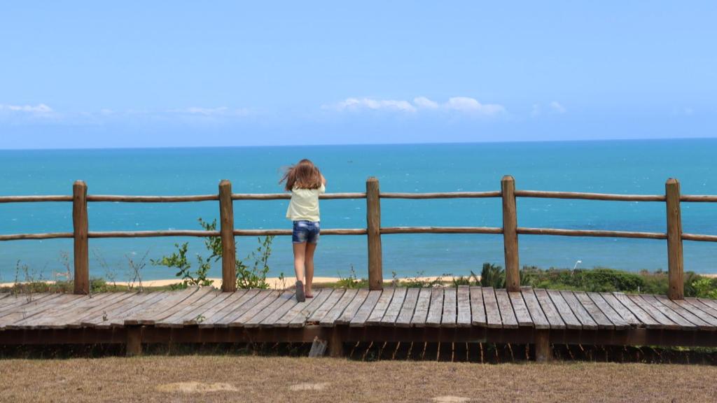 a girl standing on a wooden bridge looking at the ocean at CasAmarela in Santa Cruz Cabrália