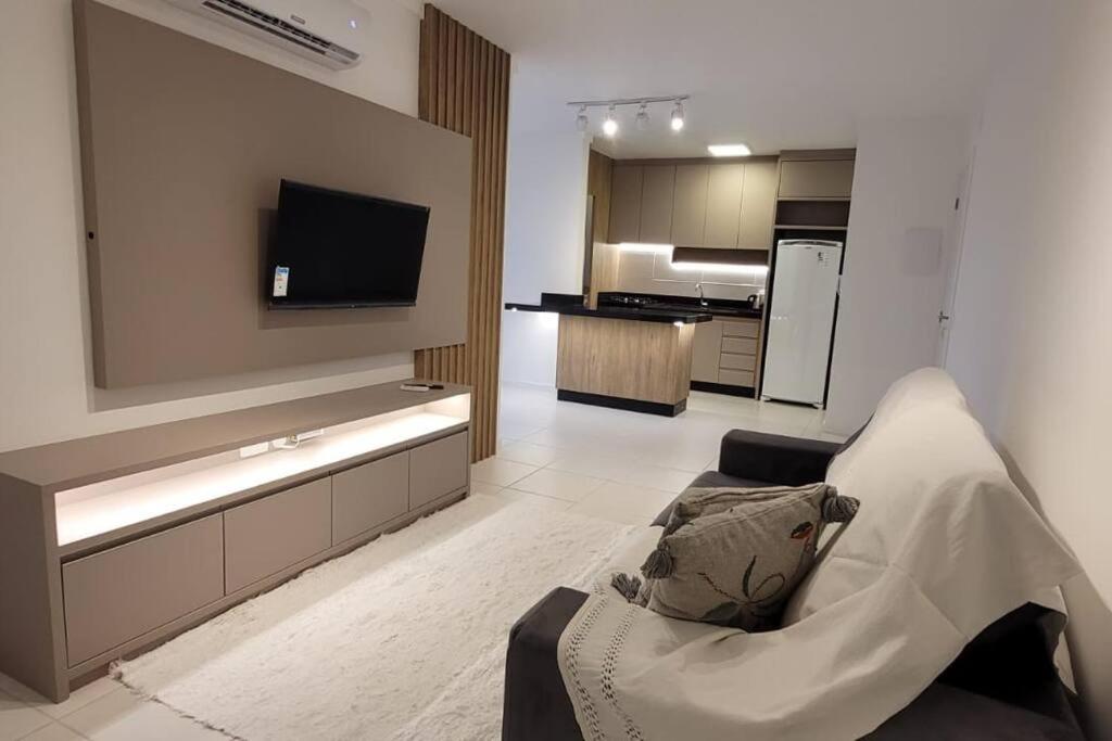 ein Wohnzimmer mit einem Sofa und einem TV sowie eine Küche in der Unterkunft Comfort Club Santorini Centro in Piçarras