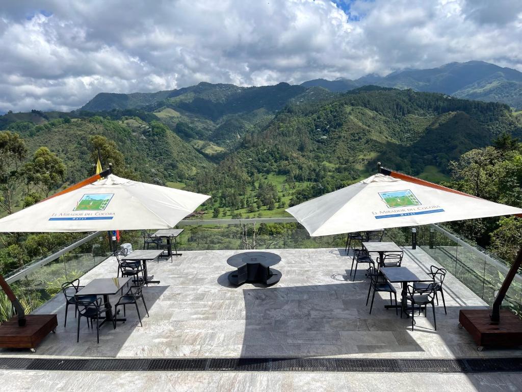 um pátio com mesas, cadeiras e guarda-sóis brancos em Hotel El Mirador del Cocora em Salento