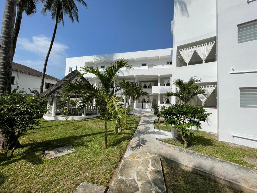 an exterior view of a white building with palm trees at Watamu Ascot Hotel in Watamu