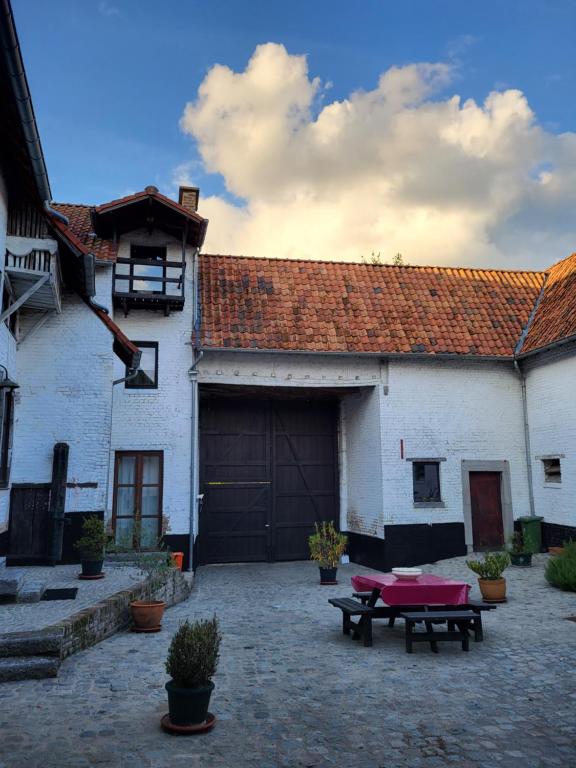 een groot wit gebouw met een garage en een picknicktafel bij Charming and cosy ART DECO house in old historic farm with private natural pool and gardens with hiking and cycling trails nearby in Sint-Truiden