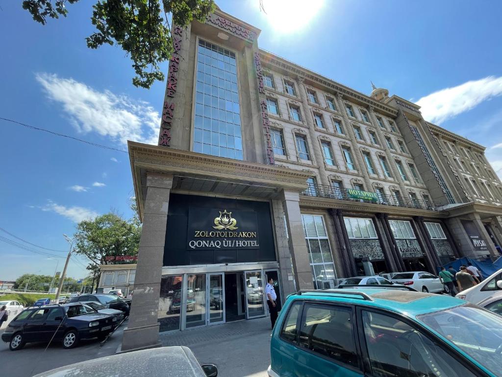un gran edificio con un coche aparcado en un aparcamiento en Zolotoi Drakon Hotel en Almaty
