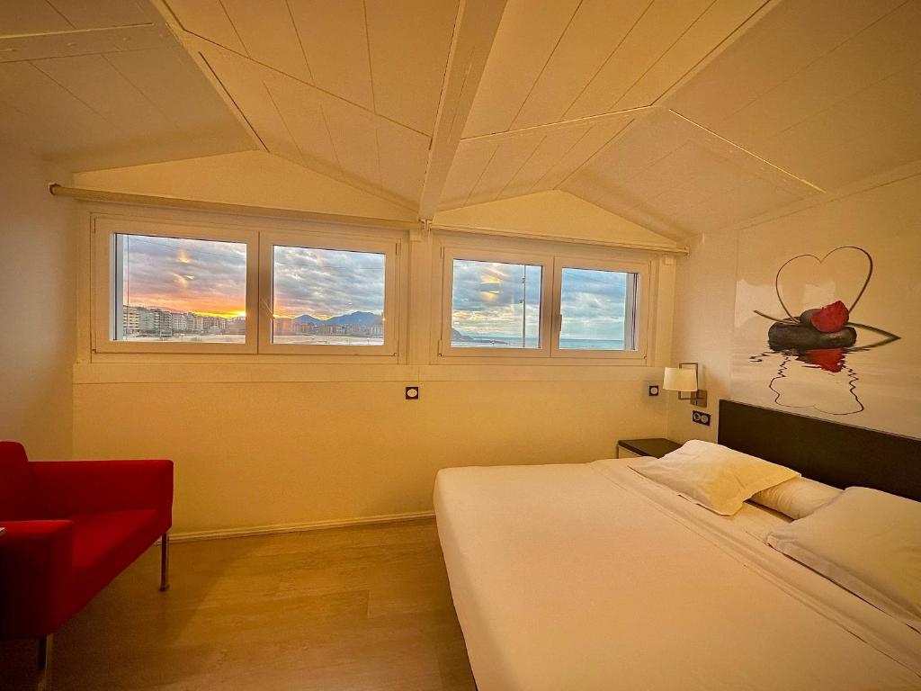 a bedroom with a bed and windows and a red chair at Hotel Punta Monpas in San Sebastián