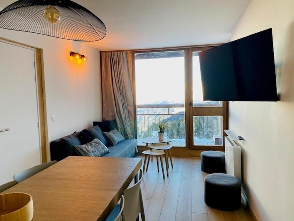 un salon avec un canapé bleu et une grande fenêtre dans l'établissement Appartement 3 pièces rénové, face Mont-Blanc, ski aux pieds, balcon, proche centre station - FR-1-346-529, à Arc 2000