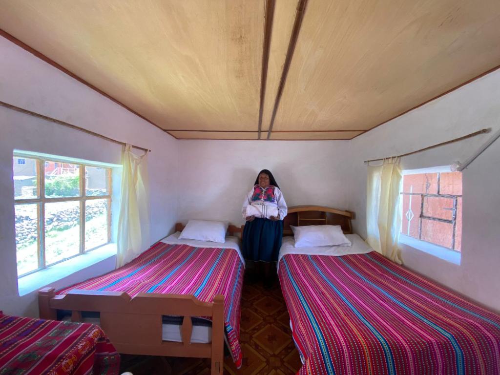 Arco Wasi Hospedaje Amantani في بونو: امرأة تقف في غرفة بسريرين