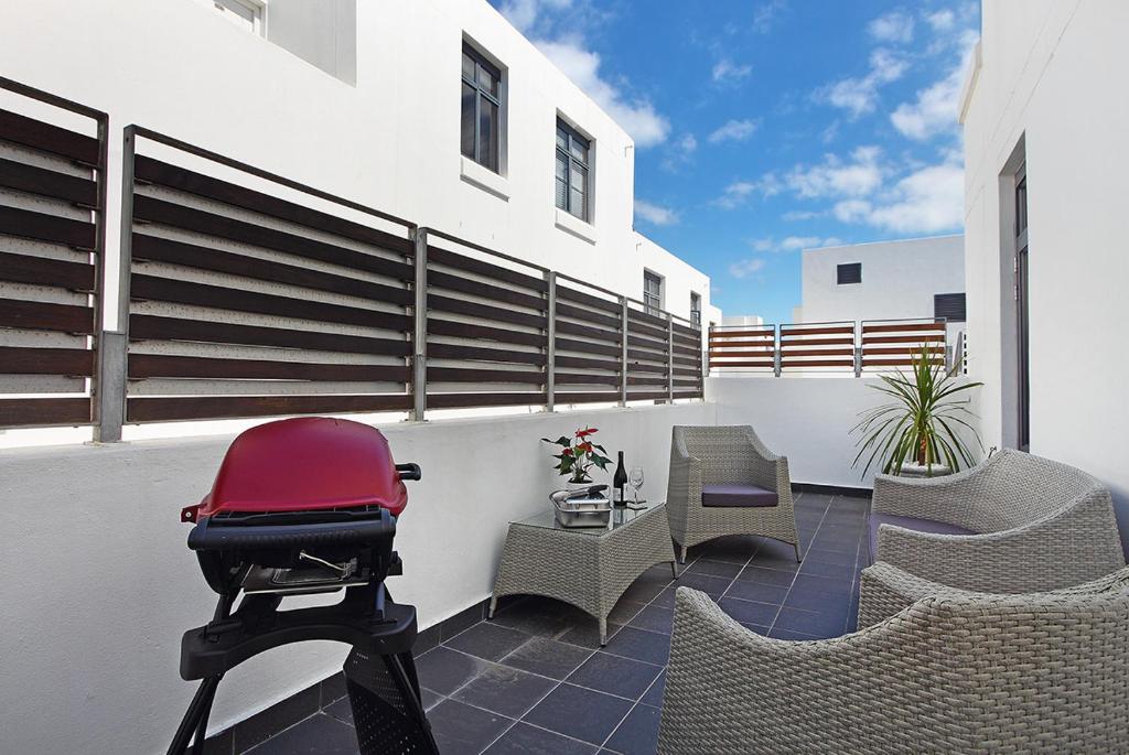 a patio with chairs and a red chair on a balcony at Eden on The Bay 125 by HostAgents in Bloubergstrand