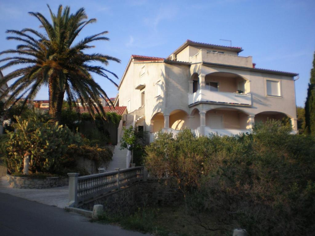 a white house with a palm tree in front of it at Guesthouse Goga in Rab