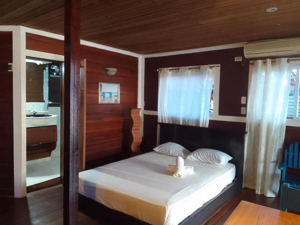 um quarto com uma cama com lençóis brancos e almofadas em Casa elba sobre el mar em Bocas del Toro