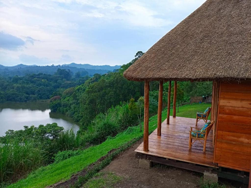 a hut with two chairs on a deck next to a river at Mwamba Kelele Lodge in Fort Portal