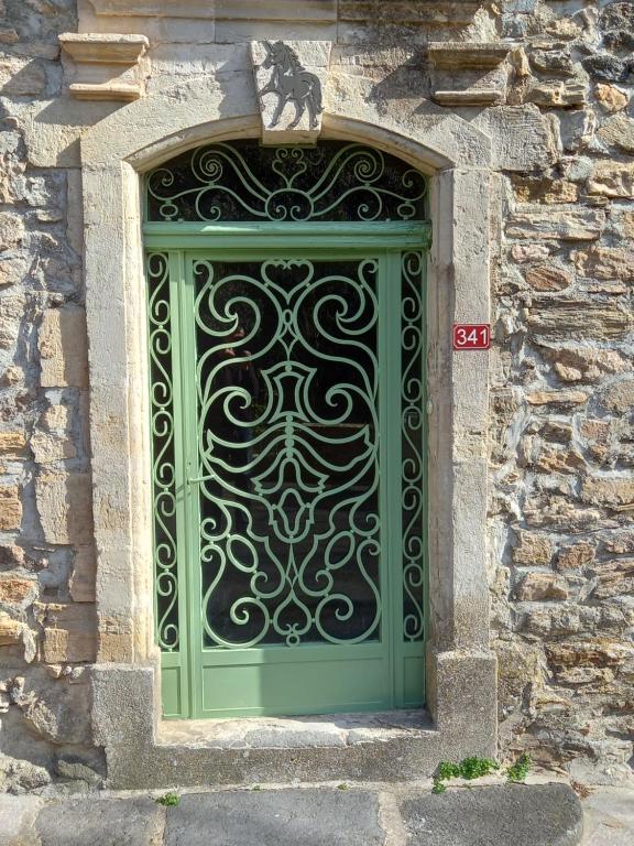 a green gate on the side of a stone building at L&#39;Armandière, maison de caractère où règne calme et sérénité. in Pézenes-les-Mines