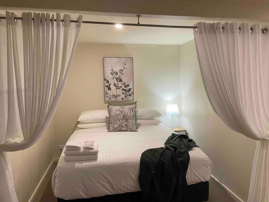um quarto com uma cama com lençóis brancos e cortinas em Elliston Cottage North Hobart x 2 em Hobart