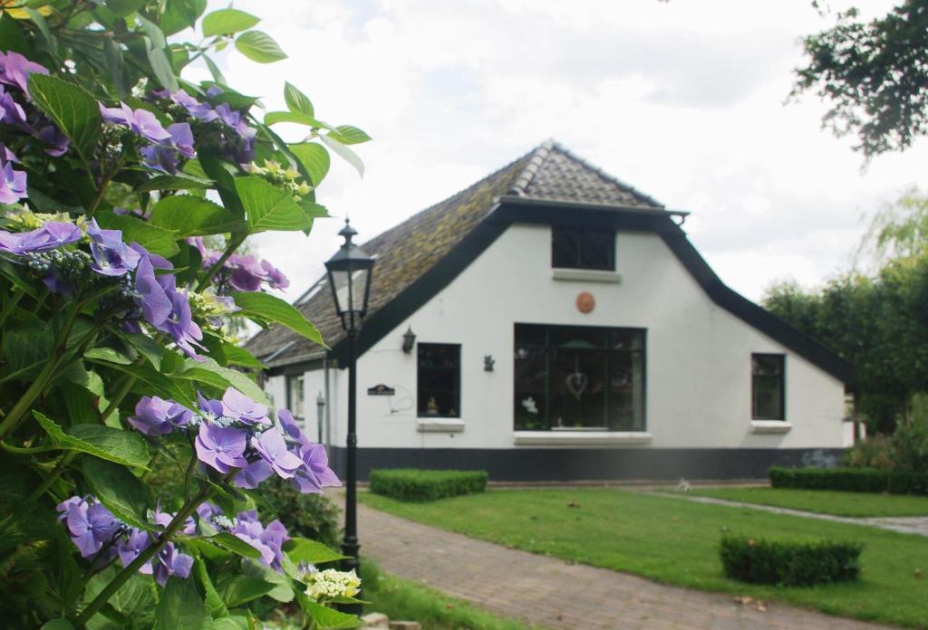 una casa blanca con flores púrpuras delante de ella en Bed&Breakfast 't Eikeltje, en Hollandscheveld