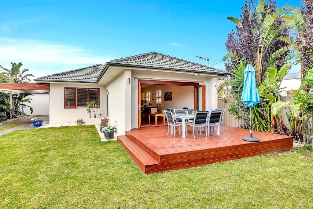 a wooden deck with chairs and an umbrella in a yard at Gladstone Gardens - Family Comfort in North Brighton in Adelaide