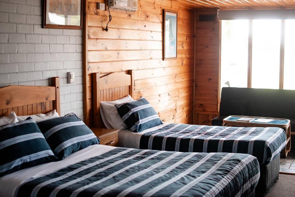 two beds in a room with wooden walls at Avon River Inn in Stratford