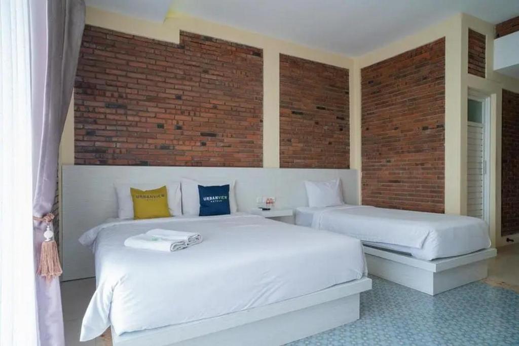 two white beds in a room with a brick wall at Urbanview Hotel Omah Anin Batu by RedDoorz in Tlekung