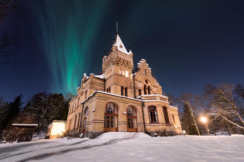 an old building with the northern lights in the sky at Merlo Slott in Timrå