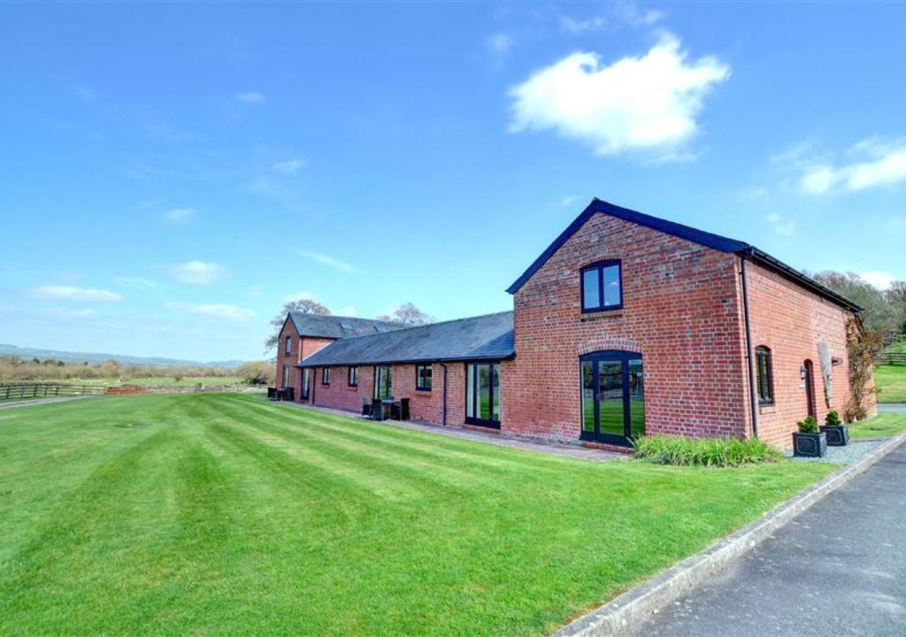 a brick house with a grass field next to a road at Y Stabl in Llandinam