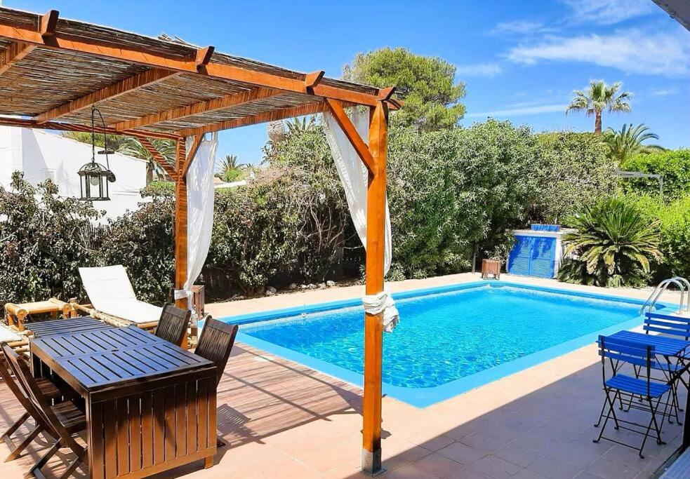 a pool with a wooden pergola and a table and chairs at ANANA Binisafua Preciosa casa al lado del mar in Binisafua