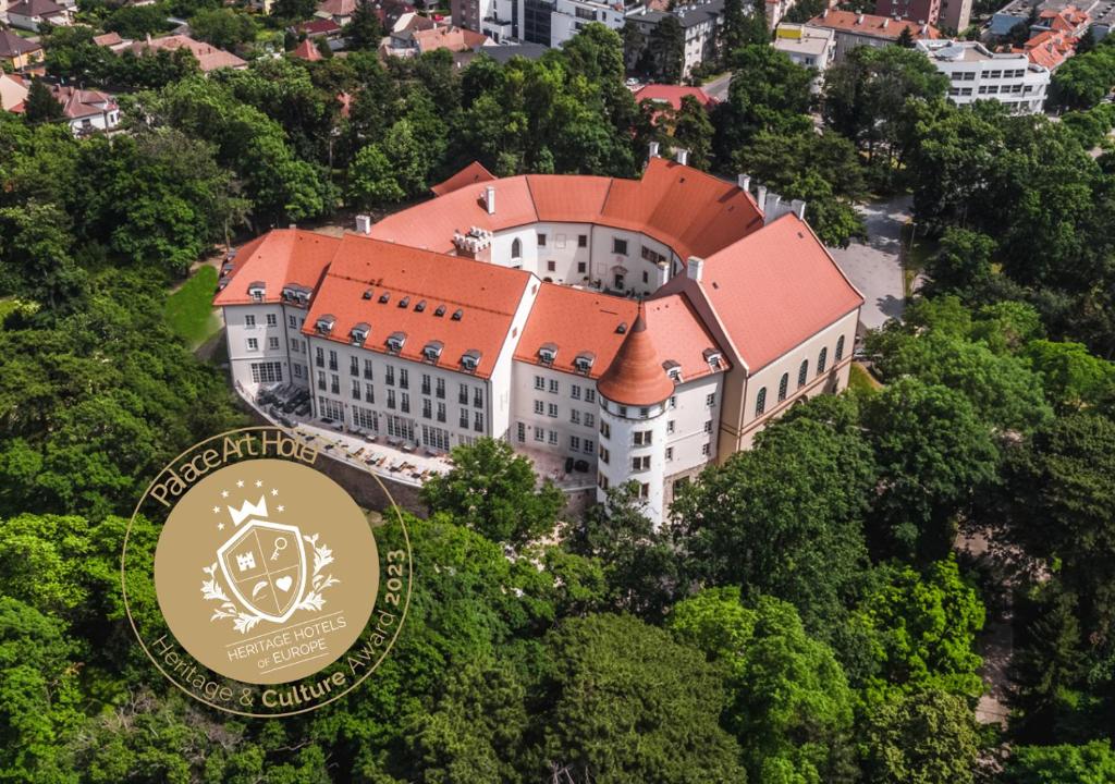 ein großes Gebäude mit rotem Dach in den Bäumen in der Unterkunft Palace Art Hotel Pezinok in Pezinok