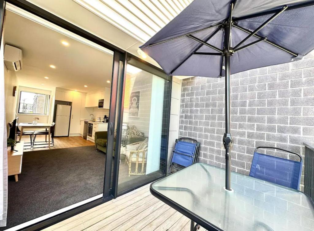 una mesa de cristal con una sombrilla en el balcón en Immaculate - 2 Bedroom Townhouse close to the train station en Auckland