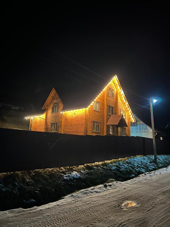 una casa de madera con luces encendidas por la noche en Котедж Mezohat, en KozÊ¼meshchek