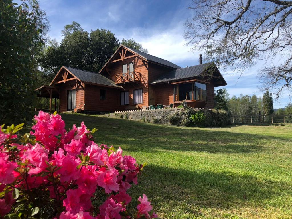 a wooden house with pink flowers in front of it at Cabañas Los Canelos Hermosa granja en Pucón in Pucón