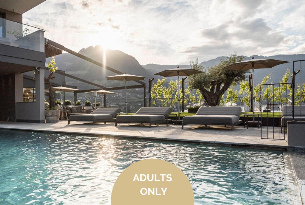 - une piscine avec des chaises et des parasols à côté d'un bâtiment dans l'établissement Vinea - Apartments, à Tirolo