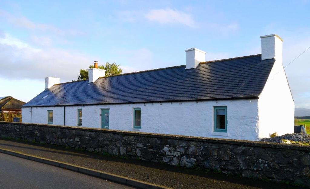 une maison blanche avec un toit noir sur un mur dans l'établissement Craigielea Cottage, à Newton Stewart