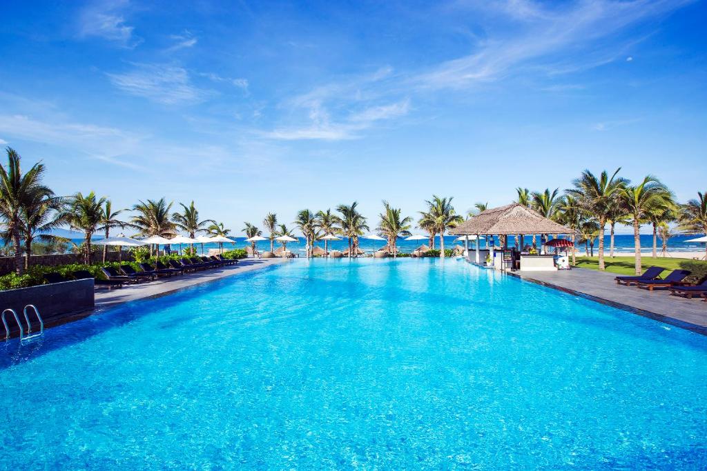 A broad daytime pool lined with loungers, umbrellas and palms.