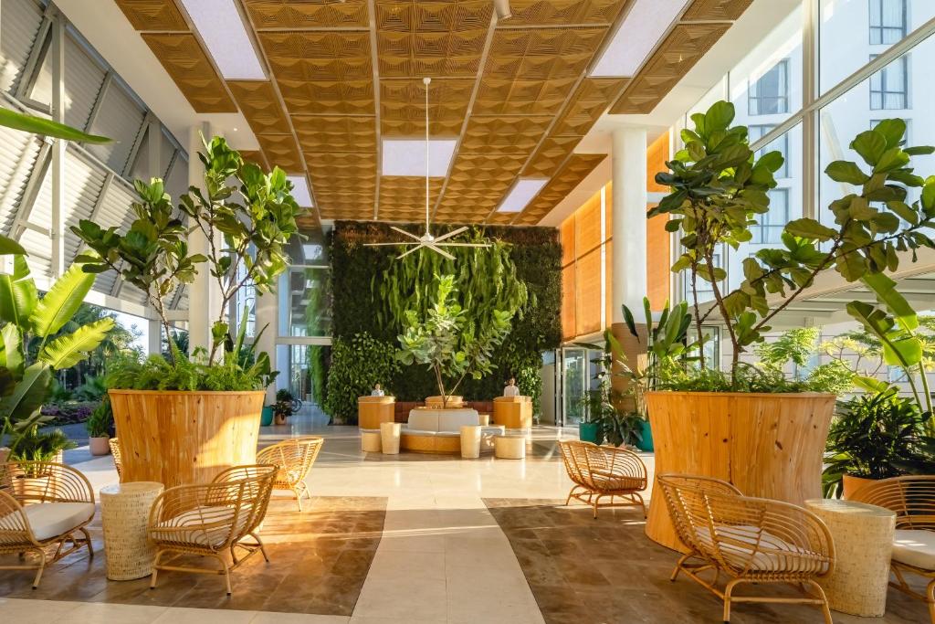 A bright, plant-filled lobby lounge with rattan seating and a high decorative ceiling.
